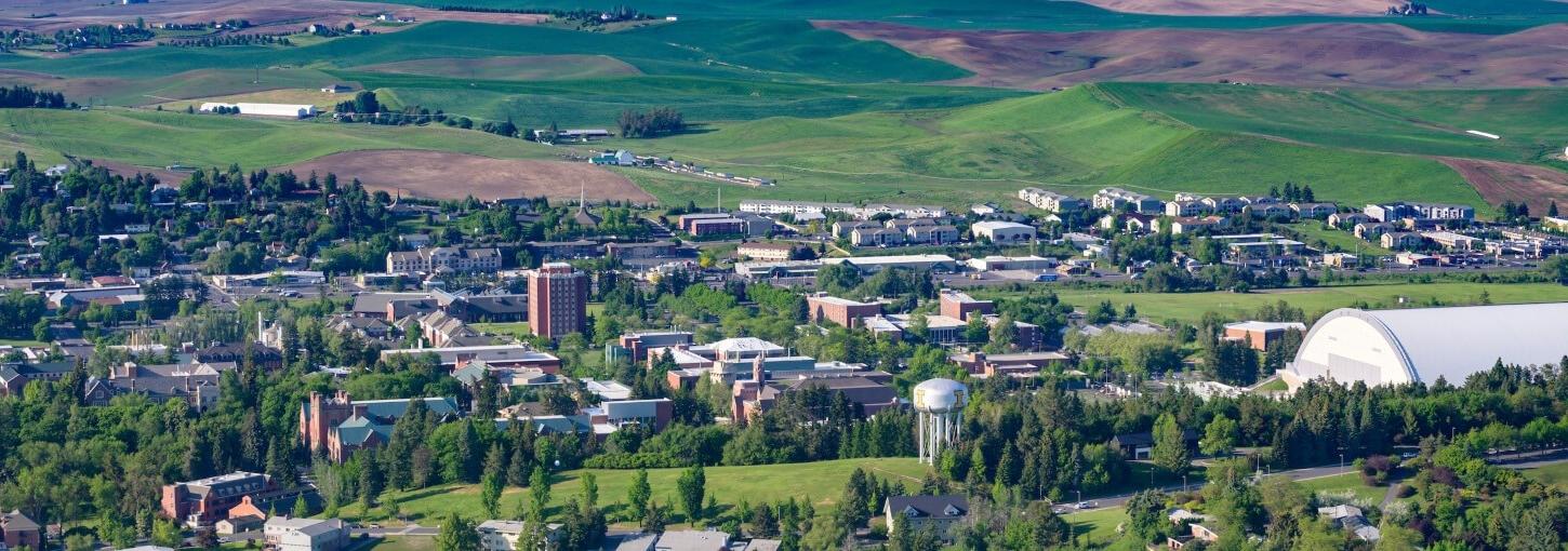 Aerial view of the University of Idaho campus with the Palouse hills in the background covered in green. 